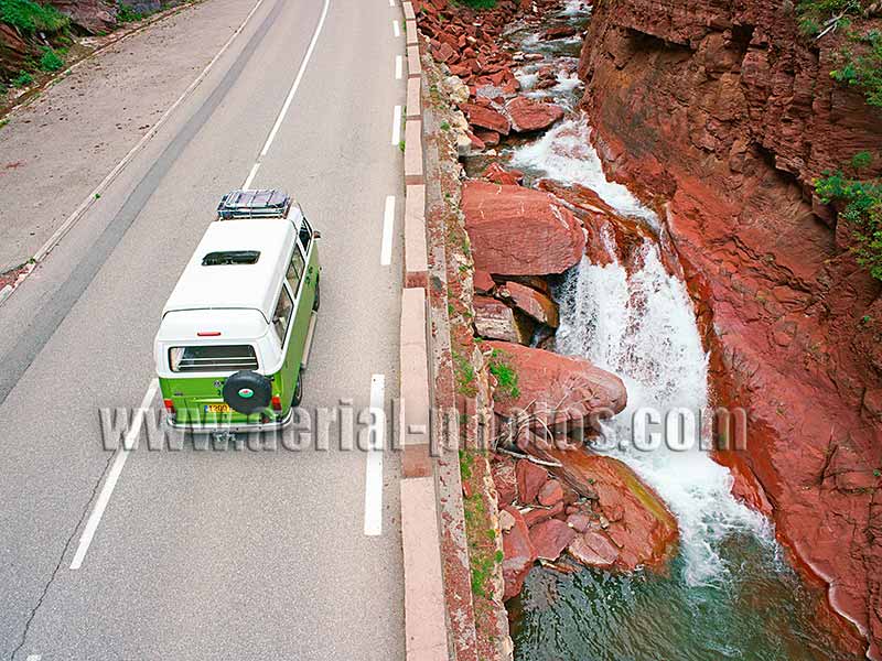 Aerial view of a Combi Volkswagen driving on a scenic route alongside a waterfall in the Alps, France. Vue aérienne.